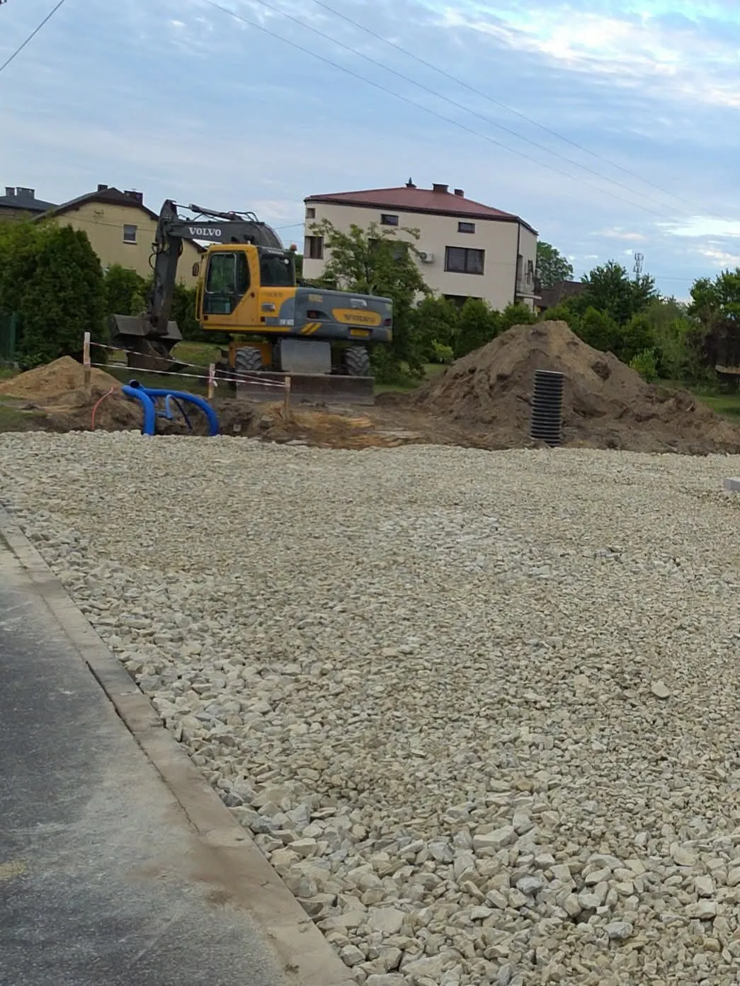 Utwardzony tłuczniem plac z widocznymi przyłączami, koparka w tle